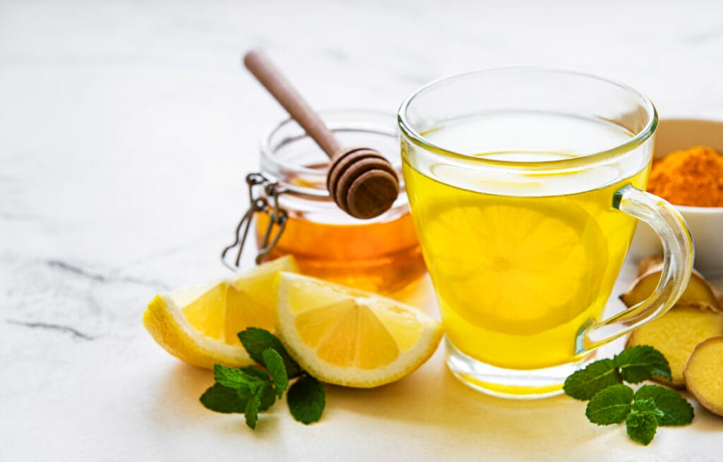 A glass of lemon water with honey and a jar of honey