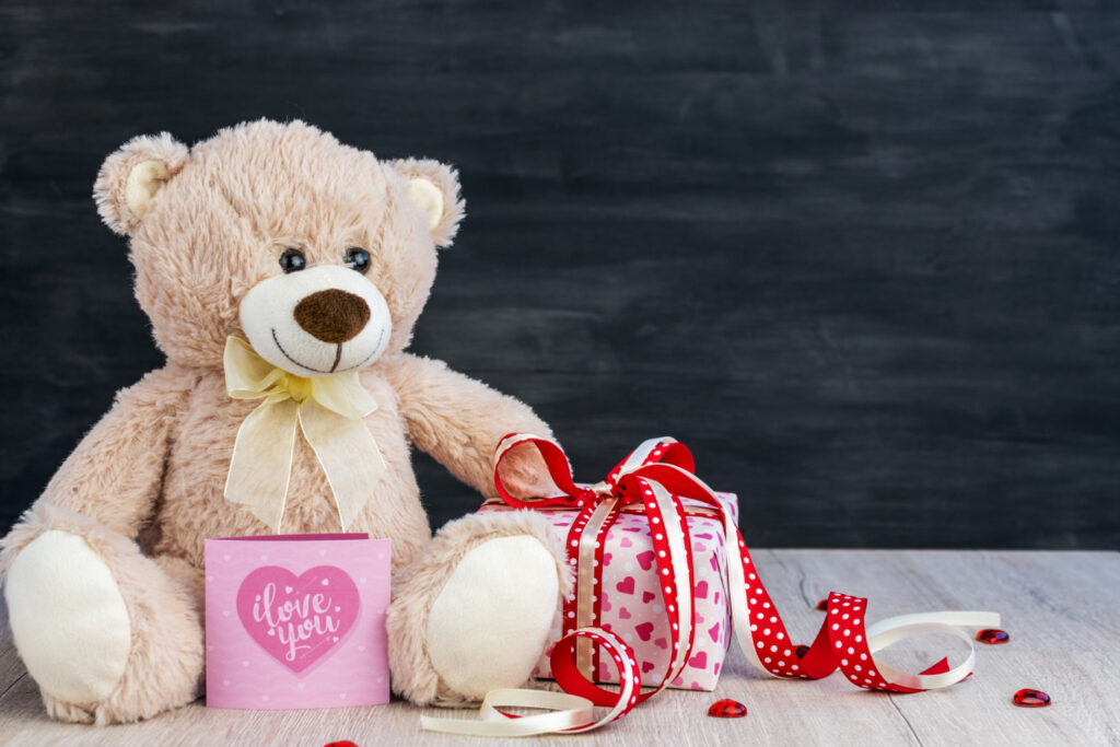 Teddy bear, gift box, greeting card and heart on a dark background